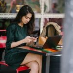 A young working woman sitting thoughtfully in a hostel room with a laptop.