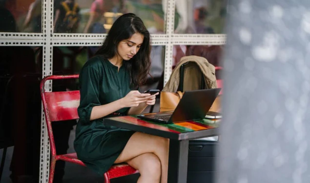 A young working woman sitting thoughtfully in a hostel room with a laptop.